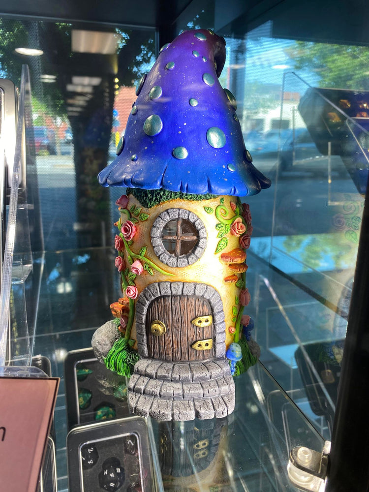 Image shows sculpted fairy house. Blue roof, pink roses, and yellow exterior.